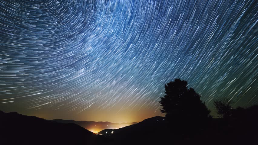 Timelapse of moving star trails in night sky. The Milky Way galaxy rotating over the mountain range in summer time