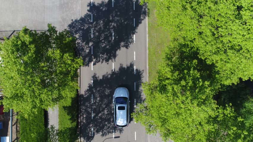 Aerial following car top-down view this grey colored station wagon also called an estate car or estate wagon has sunroof and is driving over two way street with green trees on both sides of street Royalty-Free Stock Footage #27522409