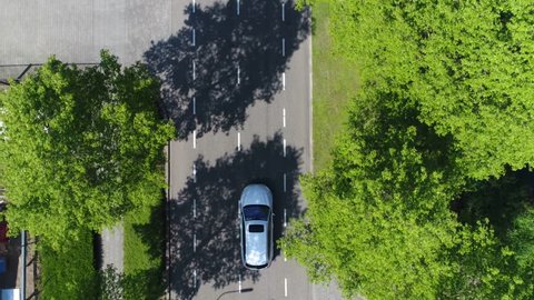 Aerial following car top-down view this grey colored station wagon also called an estate car or estate wagon has sunroof and is driving over two way street with green trees on both sides of street