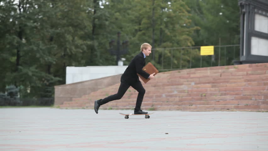 Young businessman skating on board near the building