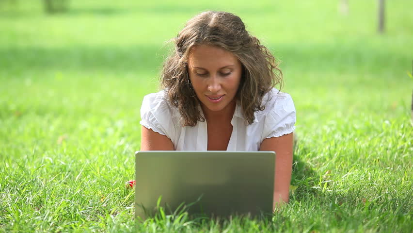 Smart businesswoman lying on the green grass and typing on the laptop