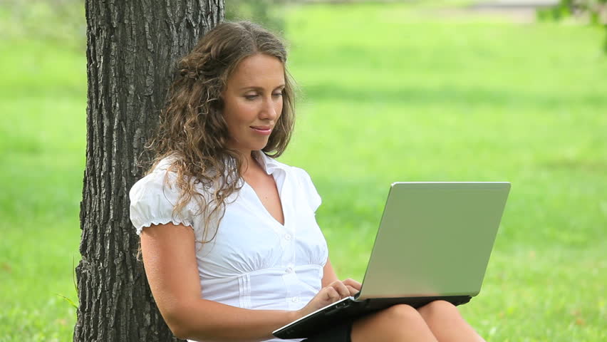 Smart businesswoman typing on the laptop near the tree