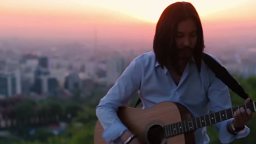 Young guitarist playing against a beautiful city landscape slow motion