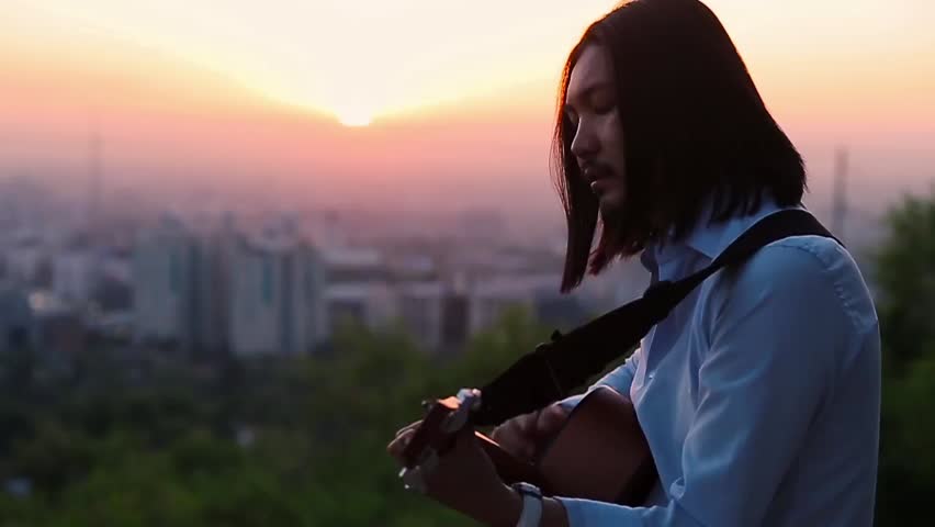 Young guitarist playing against a beautiful city landscape slow motion