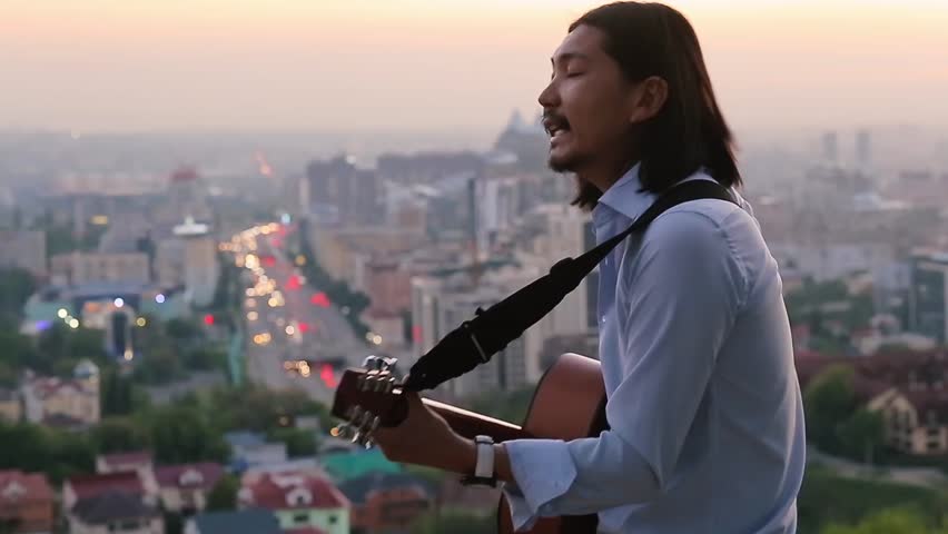 Handsome guitarist playing and singing with passion against a beautiful city landscape