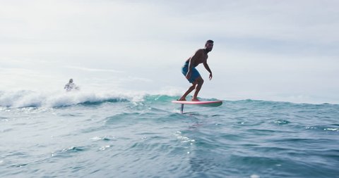 Surfer on hydrofoil surfboard riding blue ocean wave. Futuristic surfing on foil hover board.