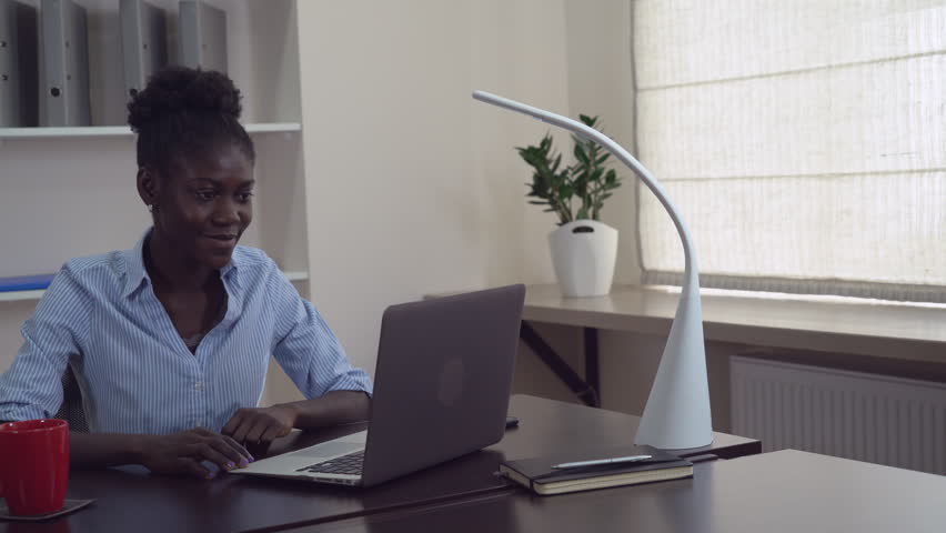 Young businesswoman has video conference call with partner or friend. Afro american manager greeting interlocutor speaking with happy smile using laptop. Cute woman sitting at the working place in Royalty-Free Stock Footage #27540625