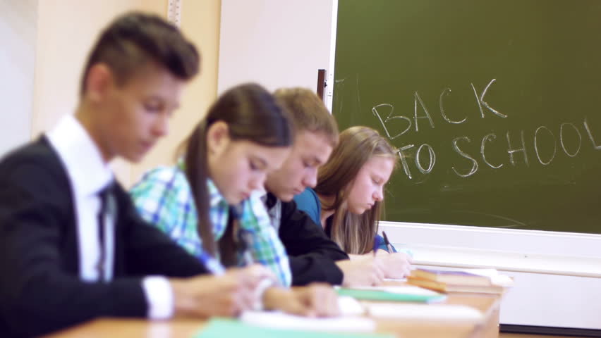 Row of four students writing task on the background of blackboard with text back