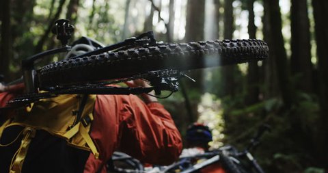 POV Medium angle shot following two mountain bikers as they hike their equipment through a redwood forest in slow motion. Wearing orange jackets. Shot in 4K on RED Epic.