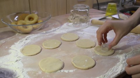 The process of cooking donuts. Female hands make a blank from the dough for a new portion of homemade doughnuts using a glass on the kitchen table.