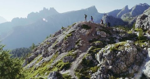 Mountain aerial flight above people hiking along trail path in sunny day. Group of friends summer adventure journey in nature outdoors. Travel exploring Alps, Dolomites, Italy. 4k drone forward video