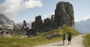Man and woman couple hiking along Cinque Torri trail path. Group of friends summer adventure journey in mountain nature outdoors. Travel exploring Alps, Dolomites, Italy. 4k slow motion video wide