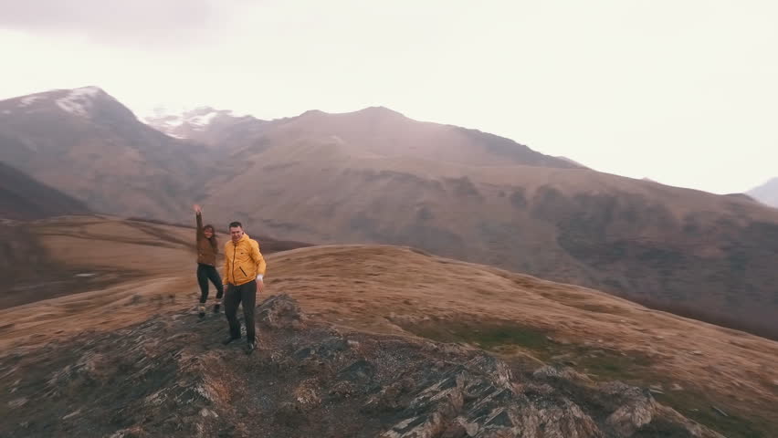 a young couple of travelers raises his arms in the background of mountains