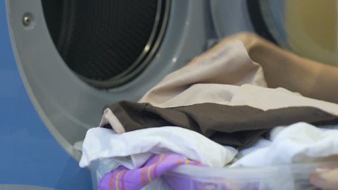Household woman carefully loading dirty clothes from basket to washing machine
