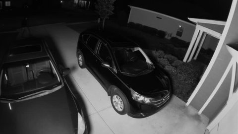 Night surveillance camera of a car thief breaking into a SUV and stealing a woman's purse in her neighborhood.    