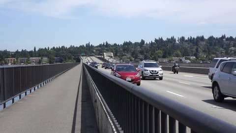 Traffic coming toward the camera heading west into Seattle, Washington on the Interstate 90 floating bridge over Lake Washington on a nice day. Also seen is the bike & walking path on side of bridge.