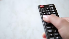 Women hand changes the channels on the TV remote control