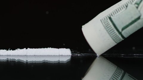 Drug Abuse. A rolled banknote snorting a line of cocaine powder. Problems with drugs concept. Black background. Close-up macro shot.