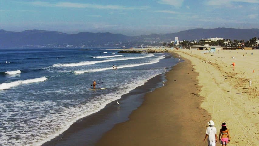 A wide shot looking down the beach at Venice Beach, CA with walkers on the shore
