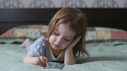 Little girl is looking at the phone. The child is playing on the smartphone. Slow motion