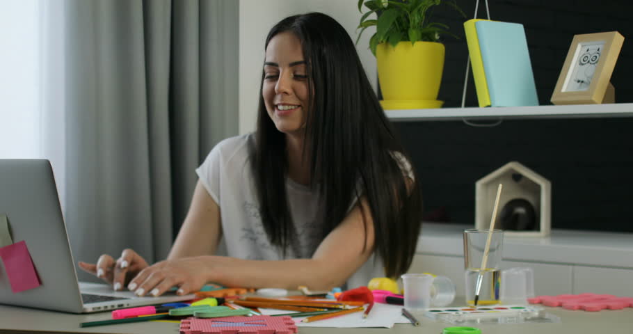 Caucasian woman with black long hair siting on the table in room while going her pretty dauther with blond curly hair. Girl giving her mother the mobile phone. Indoor.