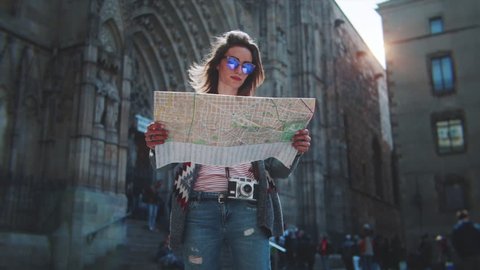 Attractive young woman traveling in Europe and exploring beautiful sightseeing in Barcelona, sunshine lens flare, slow motion, hipster girl wearing glasses and holding tourist map, enjoying holiday 
