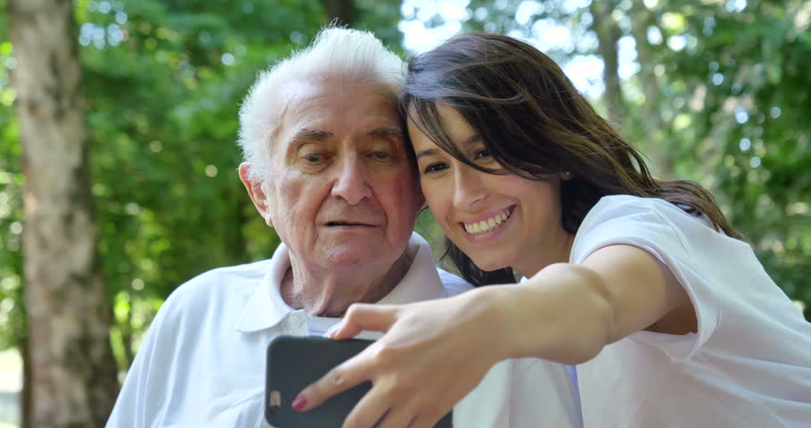 Granddaughter, a nurse, caring for the elderly, a girl (woman) and grandfather, do selfie, happy, smiles, in the park. Concept boarding house, sanatorium, house for the elderly, help for the elderly Royalty-Free Stock Footage #27590932