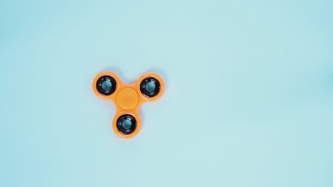 one orange fidget spinner slowly spinning on blue background, popular relaxing toy, generic design