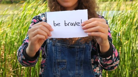 Be brave, beautiful girl showing words on nature as motivation concept