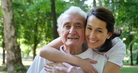 Granddaughter, nurse, caring for the elderly, girl (woman) hugging grandfather, smiling, happy, walking in the park. Concept: boarding house, sanatorium, a house for the elderly, help for the elderly.