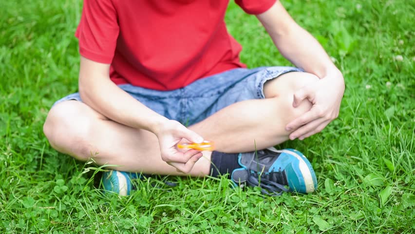 Child having fun outdoors with Spinner. Teen boy showing skills by flicking spinners with finger. Teenager in the summer park.