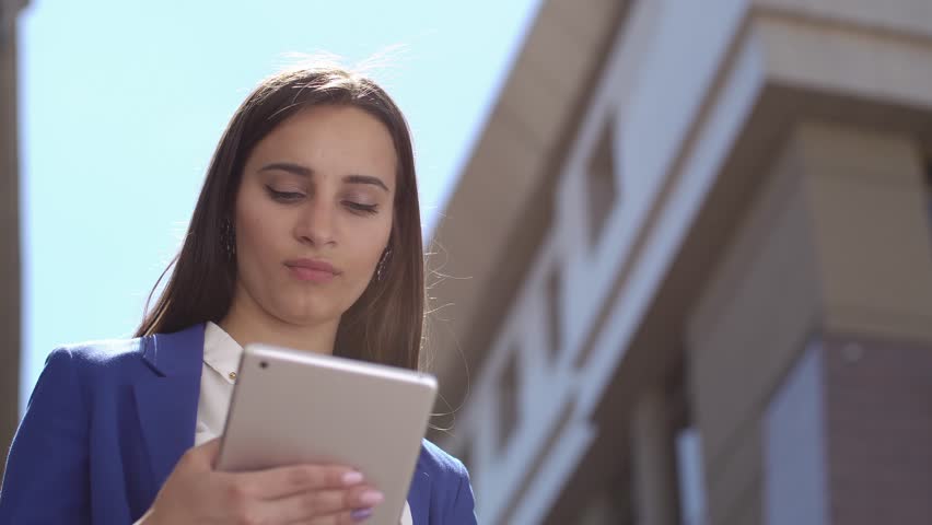 Business woman reads something on the tablet standing in the city