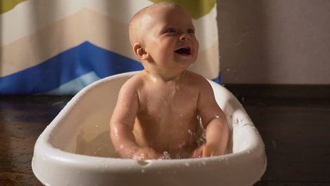Newborn baby is covered with water drops closeup playing and smiling in the bath