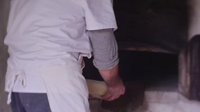Cook Engaged in Manufacturing of Bakery Products. he Shifts a Dough From a Ceramic Plate on a Wooden Shovel. With Her Help he Immerses the Dough in a Furnace. Furnace Doors Remain Opened. Video Was