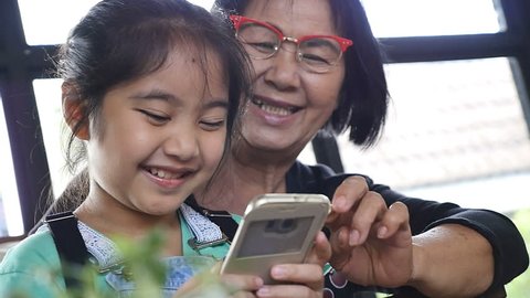 Slow motion of Little Asian girl and senior woman playing game on smart phone, Happy family concept, Pan shot.