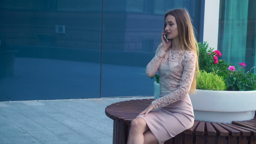 girl sitting on a circular bench near flowers and speaks on a mobile phone