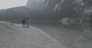 man and woman couple playing throw rocks into Braies lake. Group of friends summer adventure journey in mountain nature outdoors. Travel exploring Alps, Dolomites, Italy. 4k slow motion 60p video