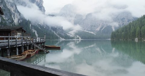 Small boathouse with wood pier and boats on Braies lake with cloudy weather.summer adventure journey in mountain nature outdoors. Travel exploring Alps, Dolomites, Italy. 4k slow motion 60p video