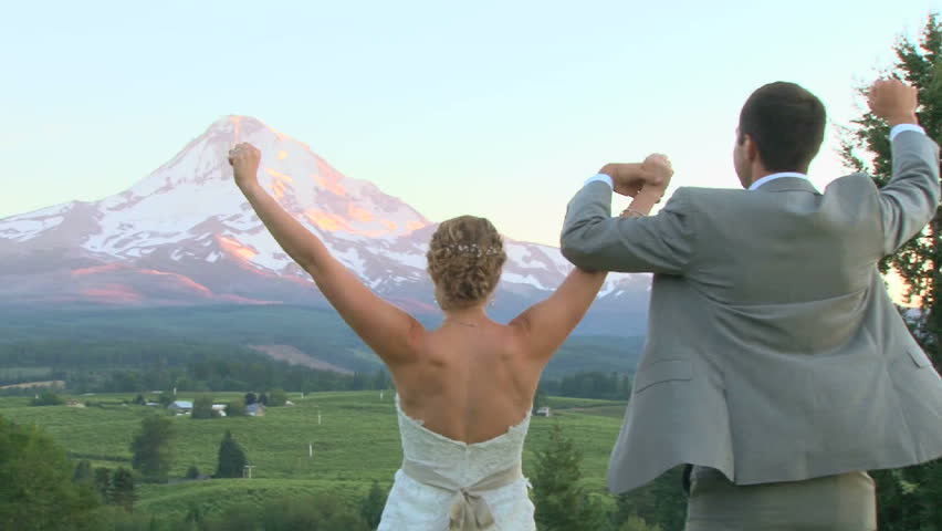Model released bride and groom lift their arms up with Mount Hood in the