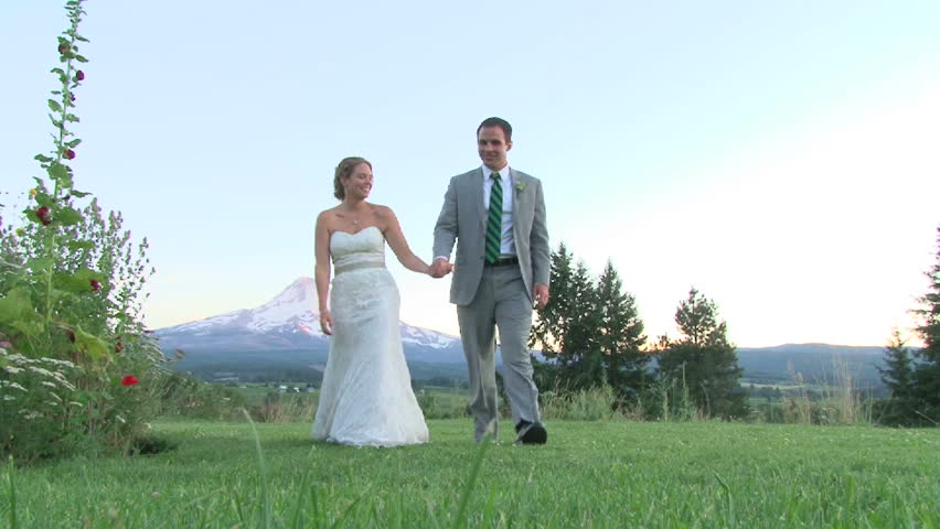 Model released bride and groom walk toward camera holding hands outdoors with Mount Hood in background.