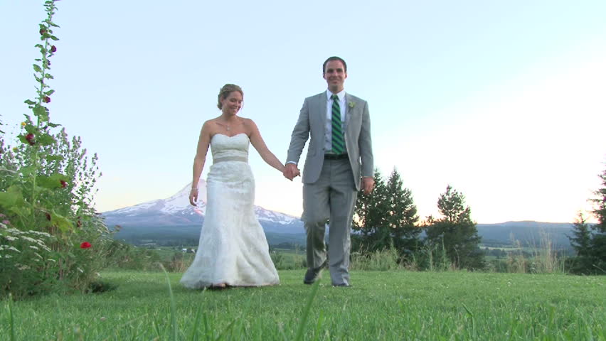 Model released bride and groom walk toward camera holding hands outdoors with