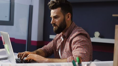 Portrait of young attractive bearded man architect working at a desk, use laptop in the office