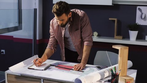 Young attractive bearded man architect working at a desk in the office