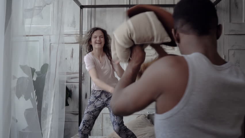 Fight by pillows of man and woman in pajamas. Loving multiethnic couple have fun, carefree morning together. Slow motion | Shutterstock HD Video #27622765