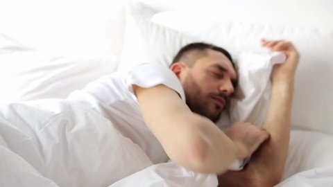 rest, sleeping and people concept - man waking up in bed at home