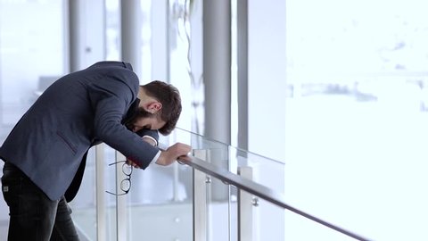 Depressed businessman bended over fence in company building and having problems