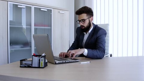 Businessman typing on laptop and looking at camera with smile