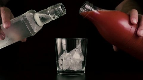 Slow motion. Male hands simultaneously pour tomato juice and vodka into a glass with ice. Cocktail bloody mary