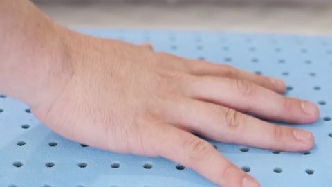 Close-up shot of a man's hand pushing down against a blue memory foam. When pressure is release, you can see the memory foam return to its original form. Shot in slow motion.