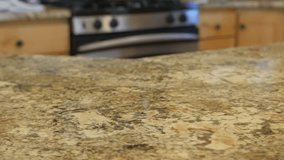 This clip features a medium shot of a granite kitchen countertop being cleaned with a blue cloth. The lady doing the cleaning sprays something over the counter before wiping it down.